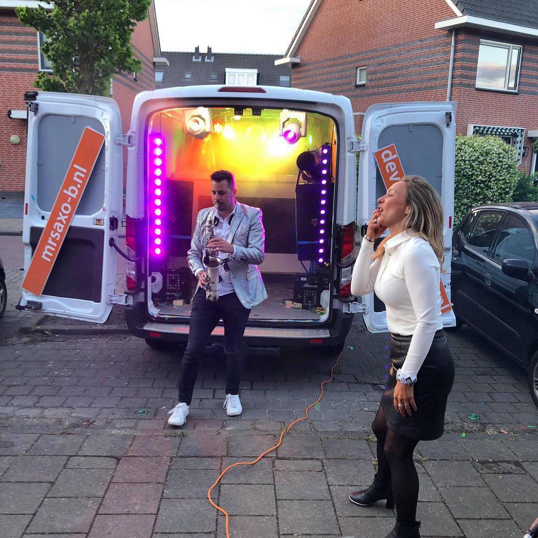 saxofonist op straat achter de discobus met een dame de feest viert