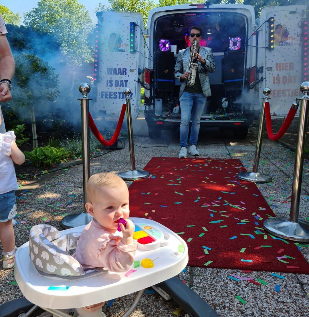 kind in kinderstoel achter d e discobus met saxofonist