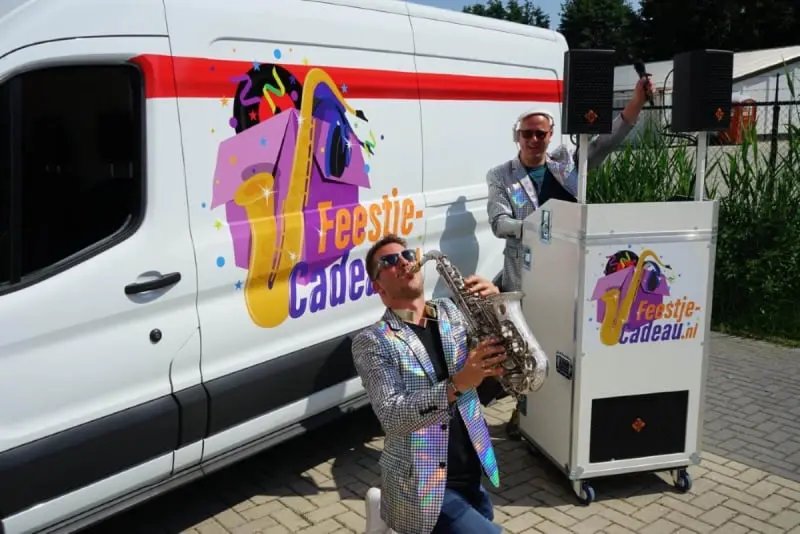saxofonist genield voor een mobiele dj booth die voor een bus staat samen met 2 mannen met een zonnenbril op
